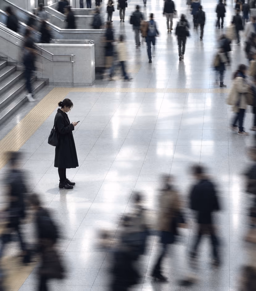 A woman standing still with her phone while commuters rush past her in a station